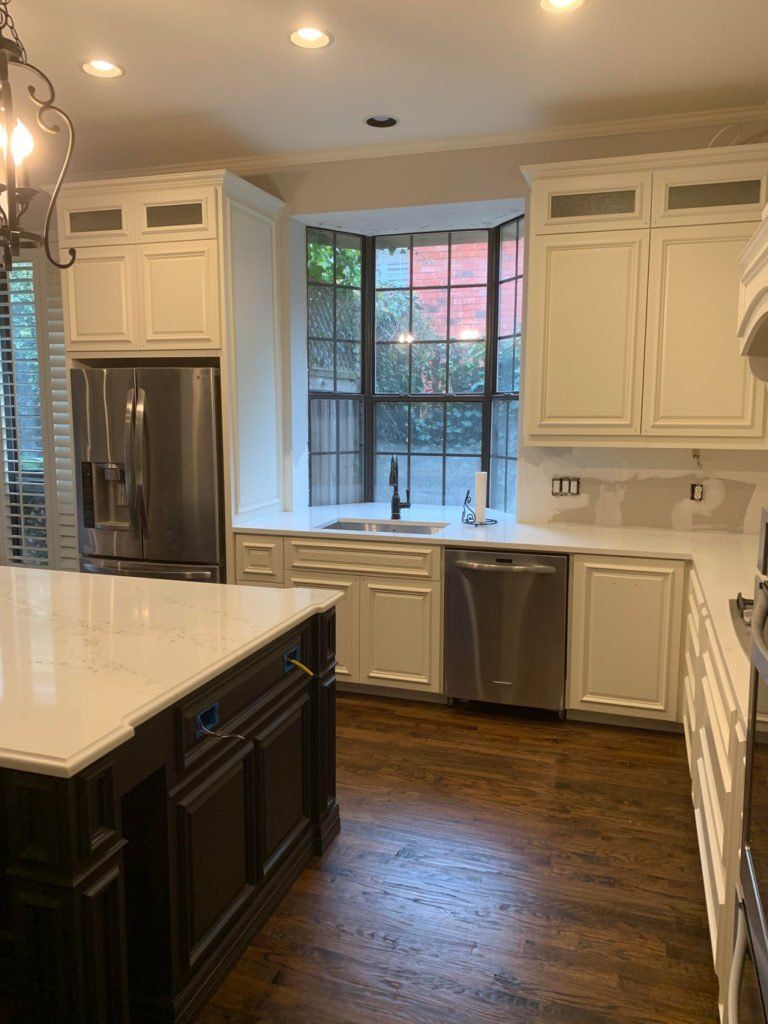 Bright kitchen with white cabinets, dark island, stainless appliances, and a window over the sink.