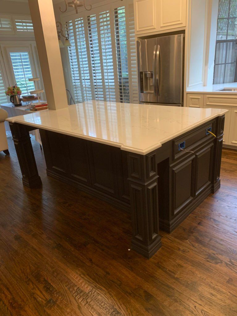 Kitchen with a large white island, dark cabinets, hardwood floors, and a stainless steel refrigerator.