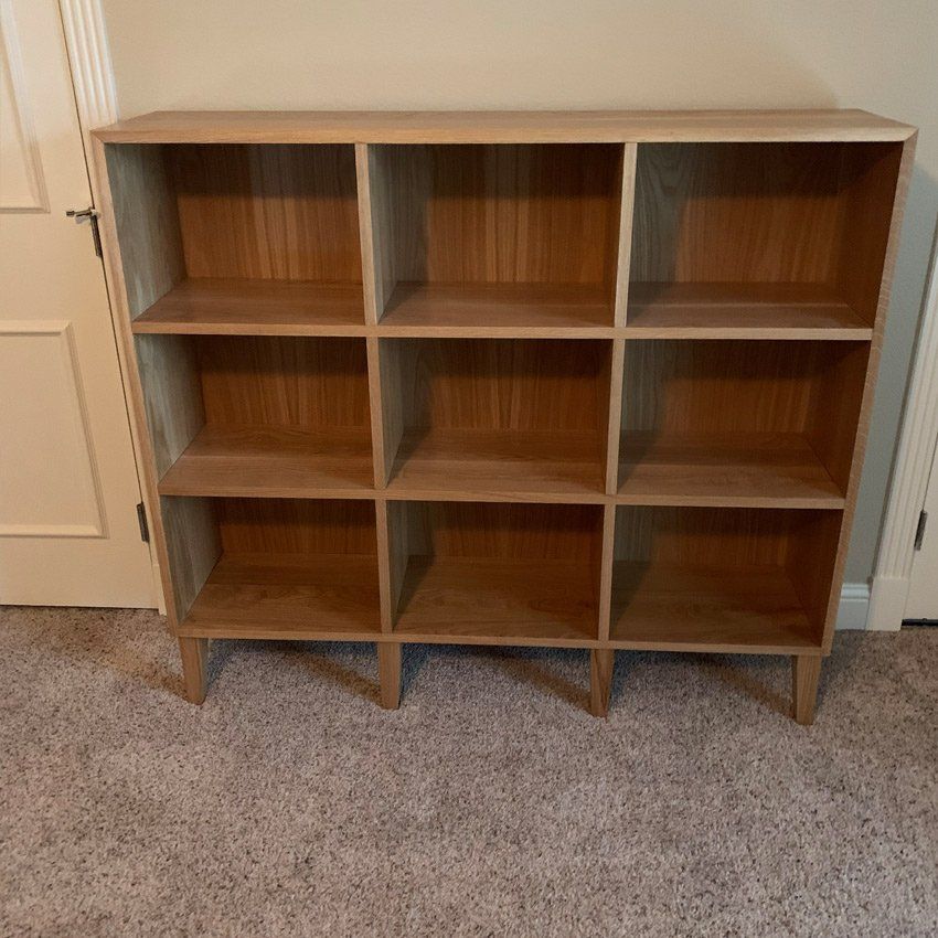 Wooden nine-cubby shelf unit against a wall on carpet, with a white door in the background