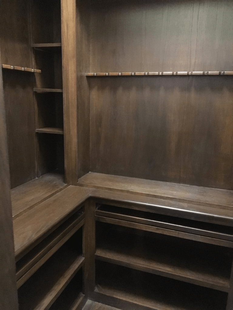Empty dark wood walk-in closet with built-in shelves and hanging rods