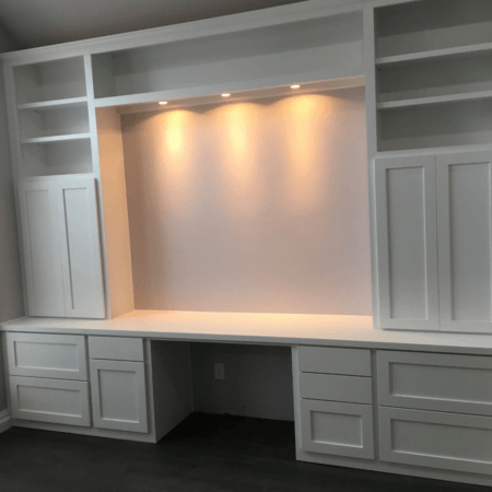 White built-in desk and cabinets with shelves, drawers, and warm recessed lighting above.