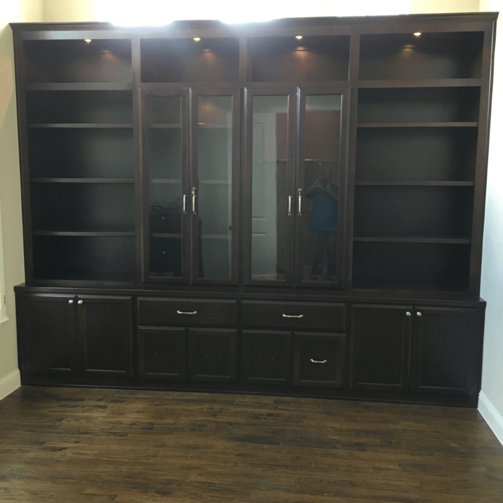Black wood built-in wall unit with shelves, glass cabinet doors, and lower storage cabinets in a room.