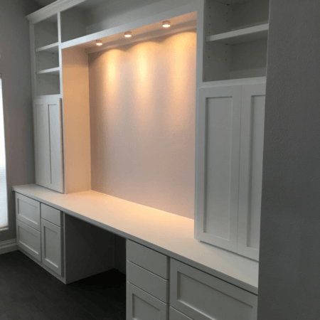 Built-in white desk nook with cabinets, shelving, and warm recessed lighting