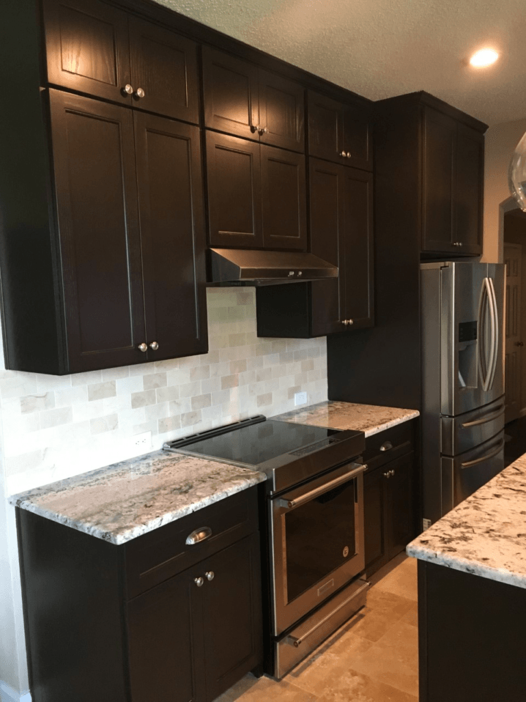 Modern kitchen with dark cabinets, granite counters, stainless steel appliances, and tile backsplash