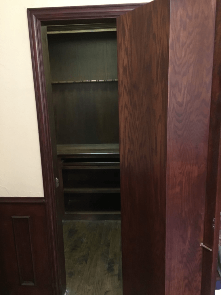 Open wooden closet with dark shelves and wood-paneled doors in a hallway
