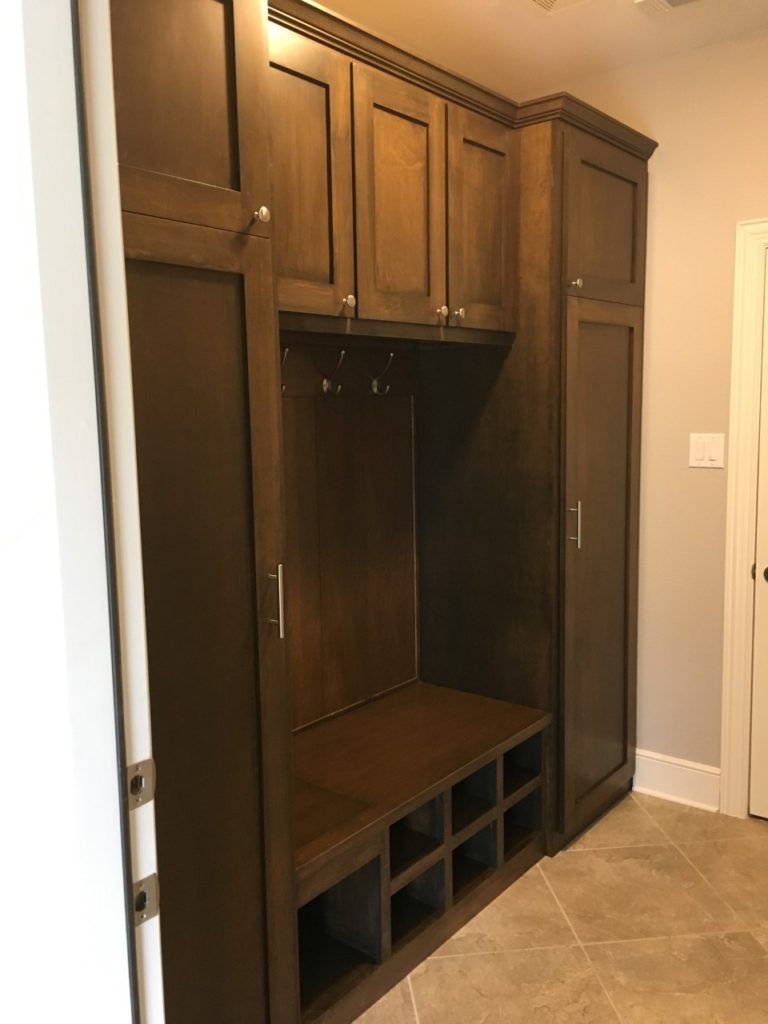Built-in dark wood mudroom cabinet with bench, hooks, and storage cubbies in a tiled entryway