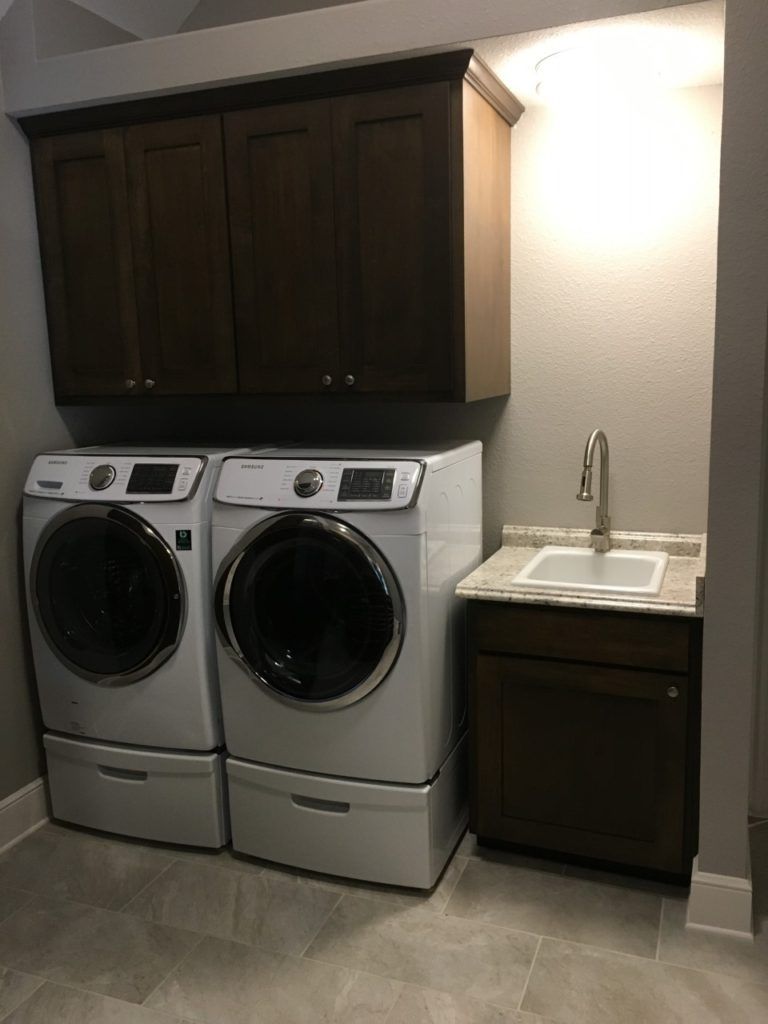 Laundry room with stacked washer and dryer, dark cabinets, and a utility sink under a bright wall light