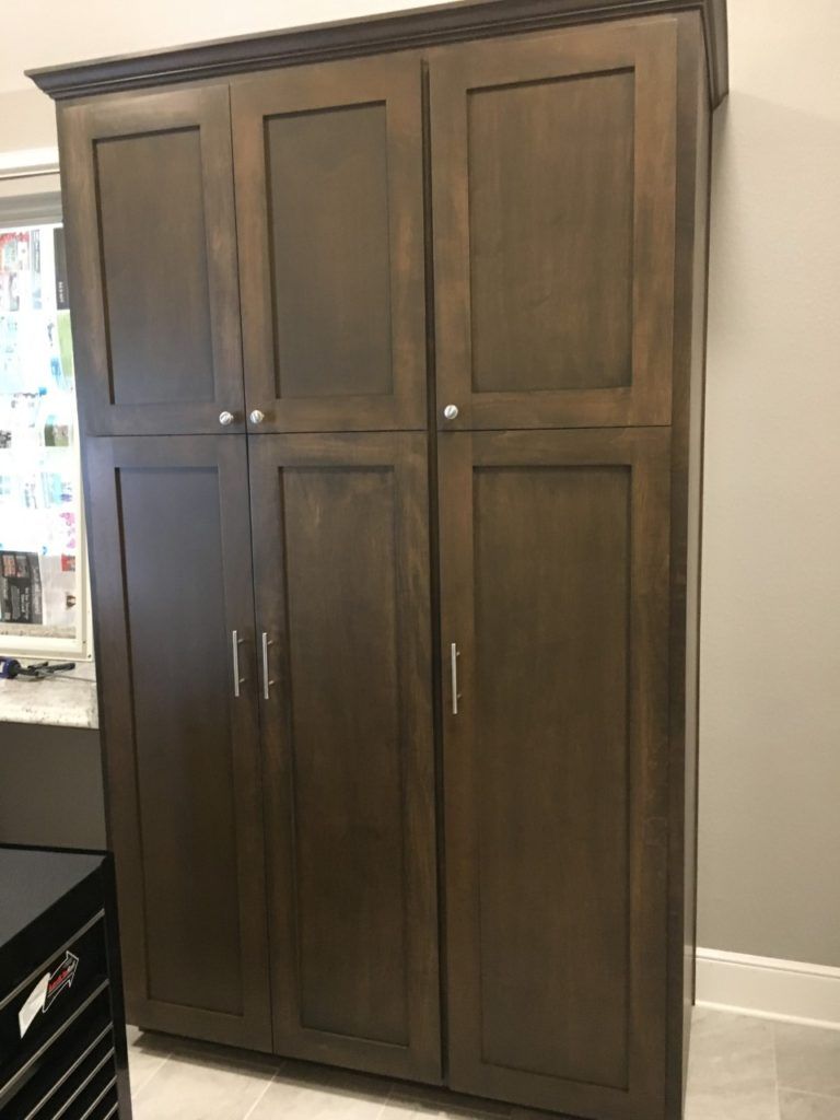 Dark wood storage cabinet with four paneled doors against a light wall in a room