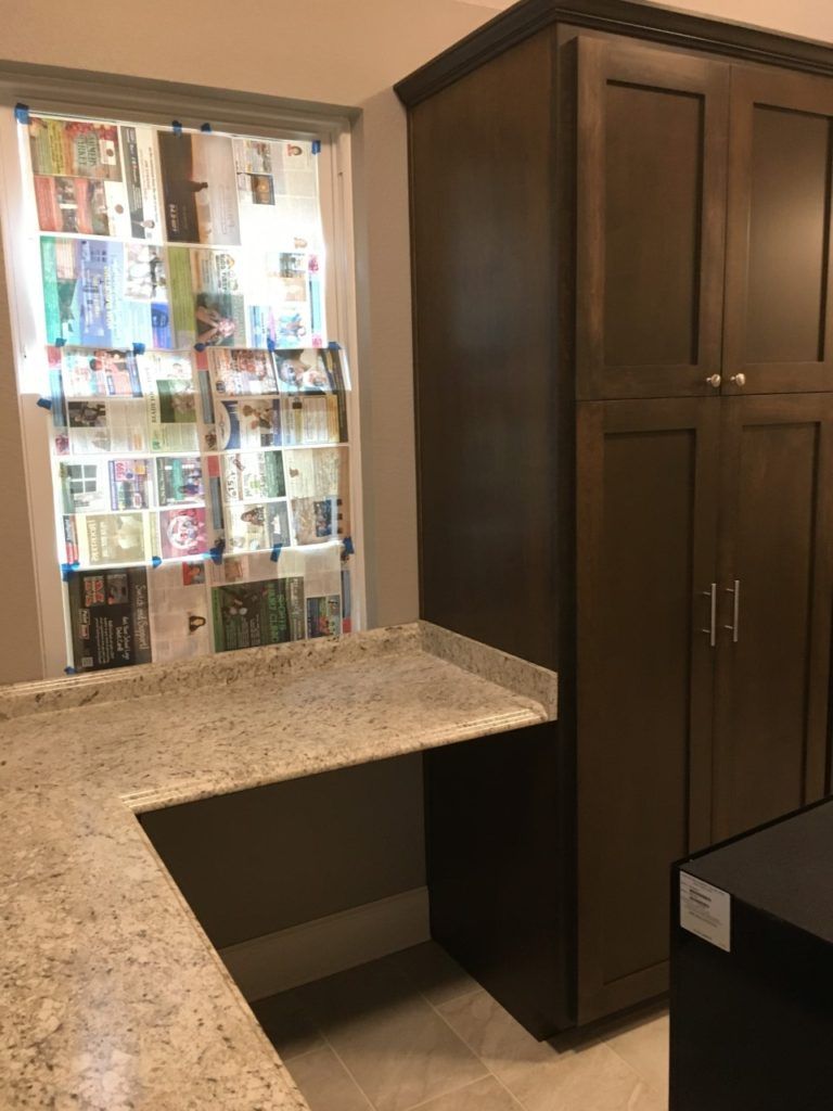 Kitchen counter beside dark wood cabinet and window with colorful hanging papers.