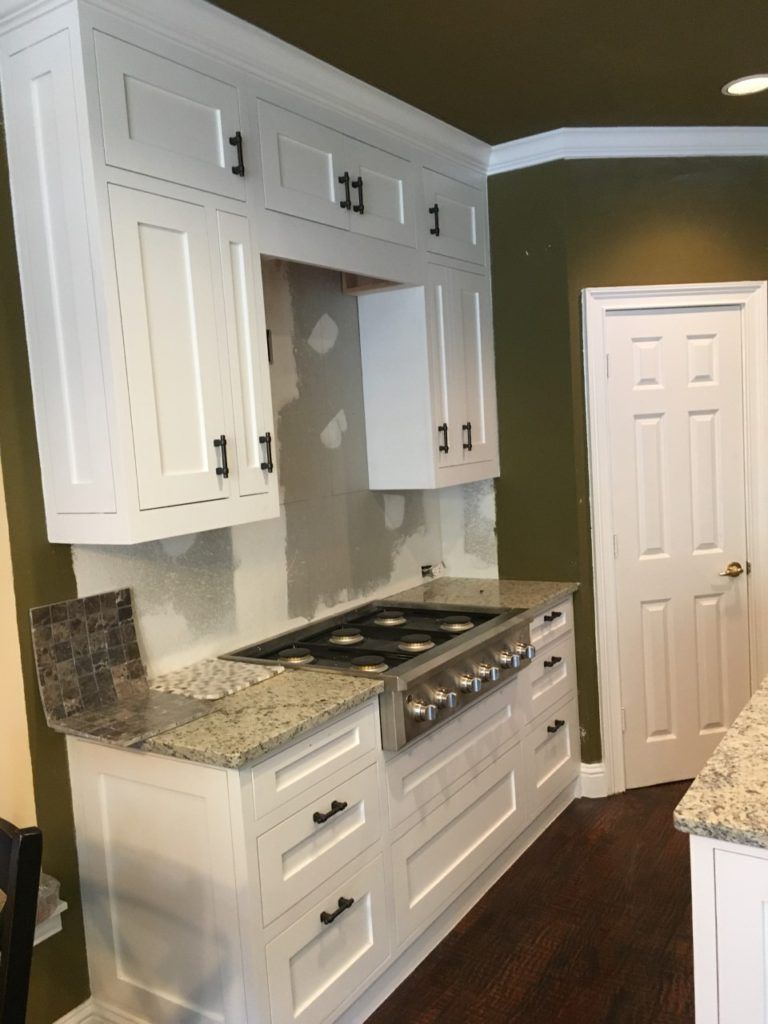 White kitchen with granite counters, built-in stovetop, and olive green accent wall beside a doorway