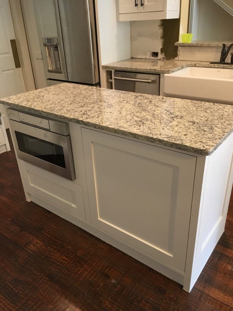 Kitchen island with white cabinets, granite countertop, and built-in microwave in a modern kitchen.