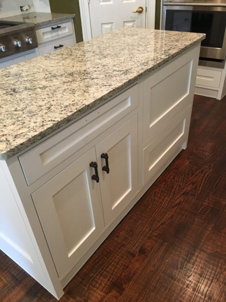 Kitchen island with white cabinets and speckled granite countertop on dark wood floor