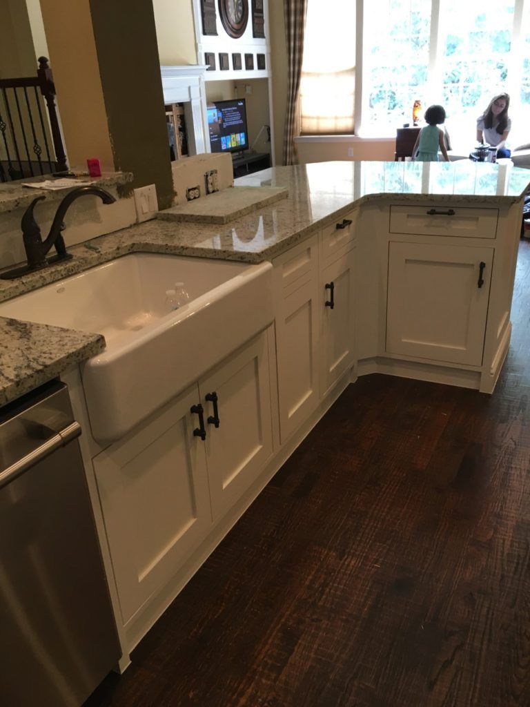 Kitchen with white cabinets, granite island, and dark wood floor, leading to a bright dining area.