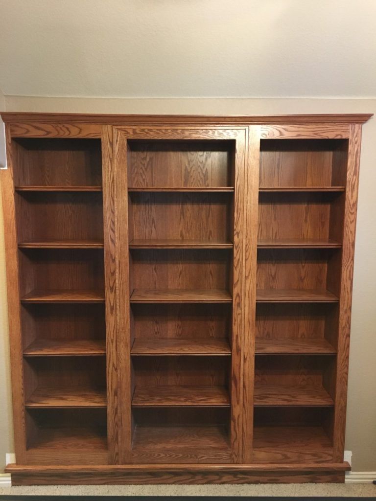 Empty wooden bookshelf with three columns and multiple shelves against a beige wall.