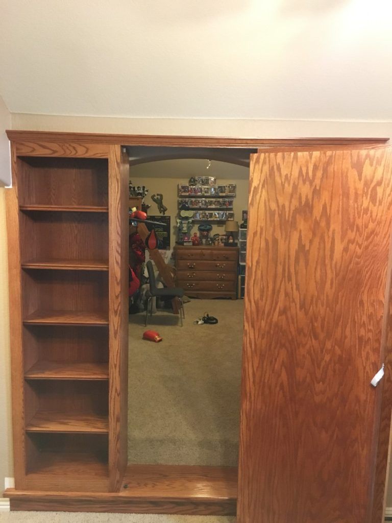 Wooden wardrobe with mirrored sliding door, opening to a cluttered carpeted bedroom beyond.