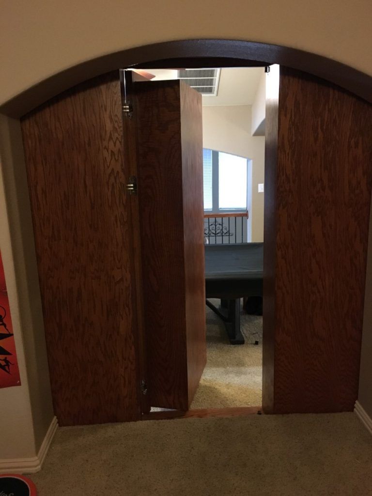 Open wooden double doors leading to a room with a pool table and windows inside.