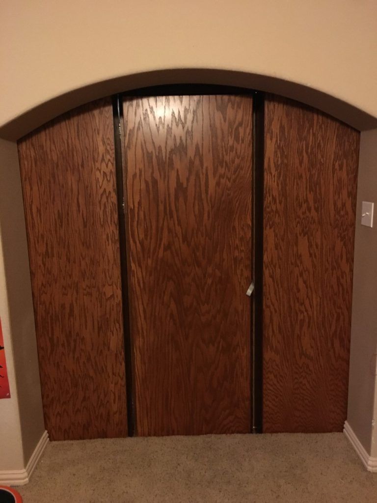 Brown arched double closet doors with vertical wood grain in a beige hallway