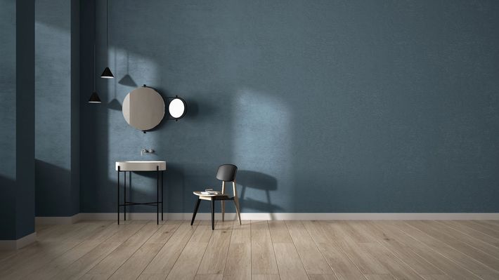 Stanza con pareti blu, lavandino, specchio e sedia, pavimento in legno e lampade a sospensione.