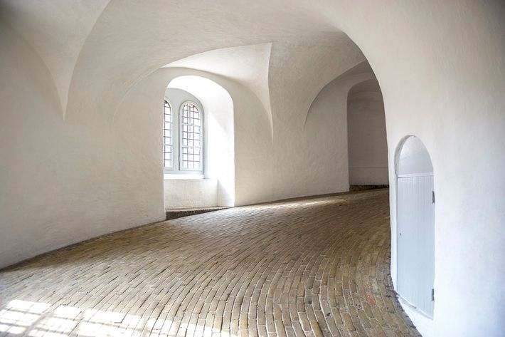 Corridoio bianco ad arco con pavimento in ciottoli e una finestra.