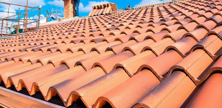 Tetto in tegole di terracotta con camino e cielo azzurro sullo sfondo.