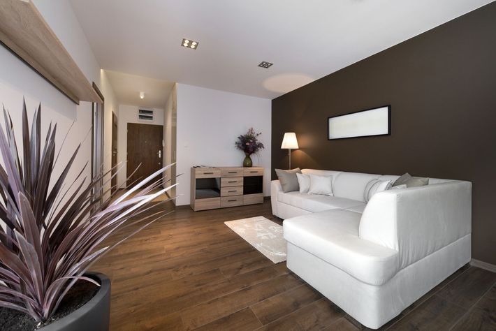 Soggiorno moderno con divano bianco, parete decorativa marrone, pavimento in legno e pianta.