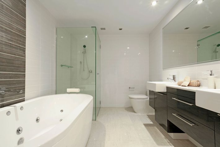 Moderno bagno bianco con vasca, doccia, WC, doppio lavabo e pannello decorativo a parete.