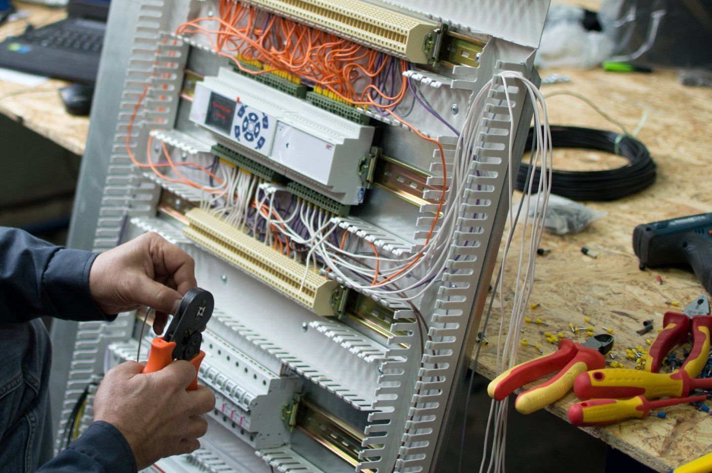 Persona che cabla il quadro elettrico con utensili arancioni e gialli. I cavi sono organizzati.