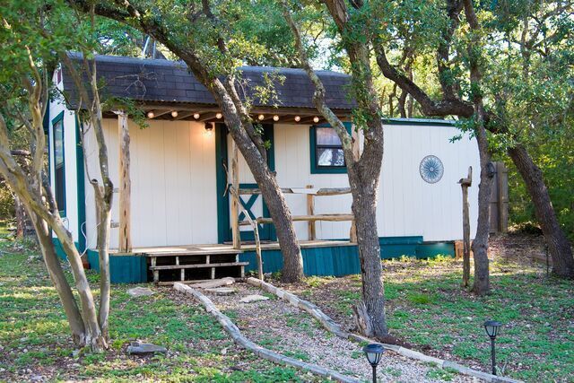 A small white and green house is surrounded by trees.