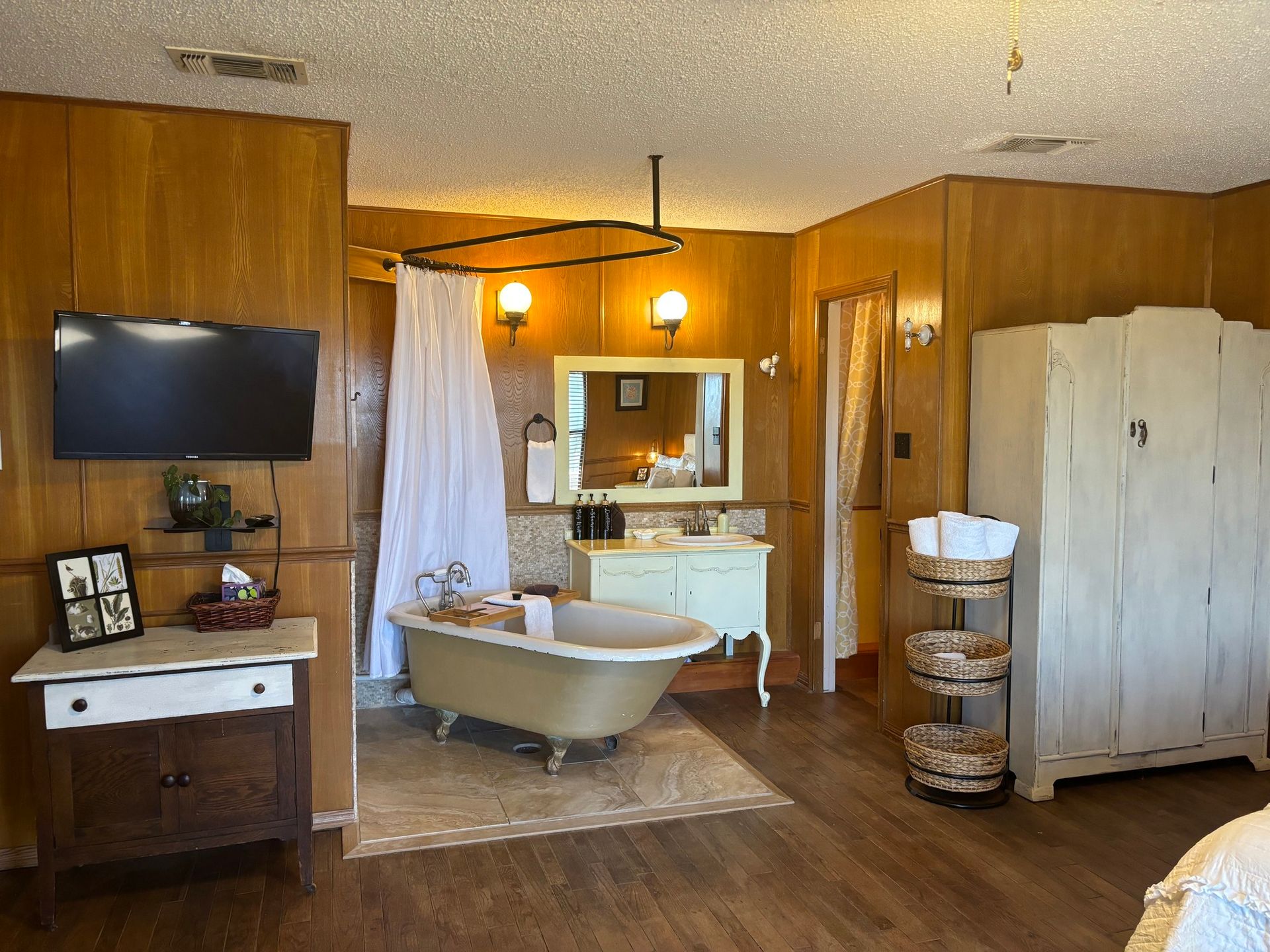 A bathroom with a tub , sink , mirror and television.