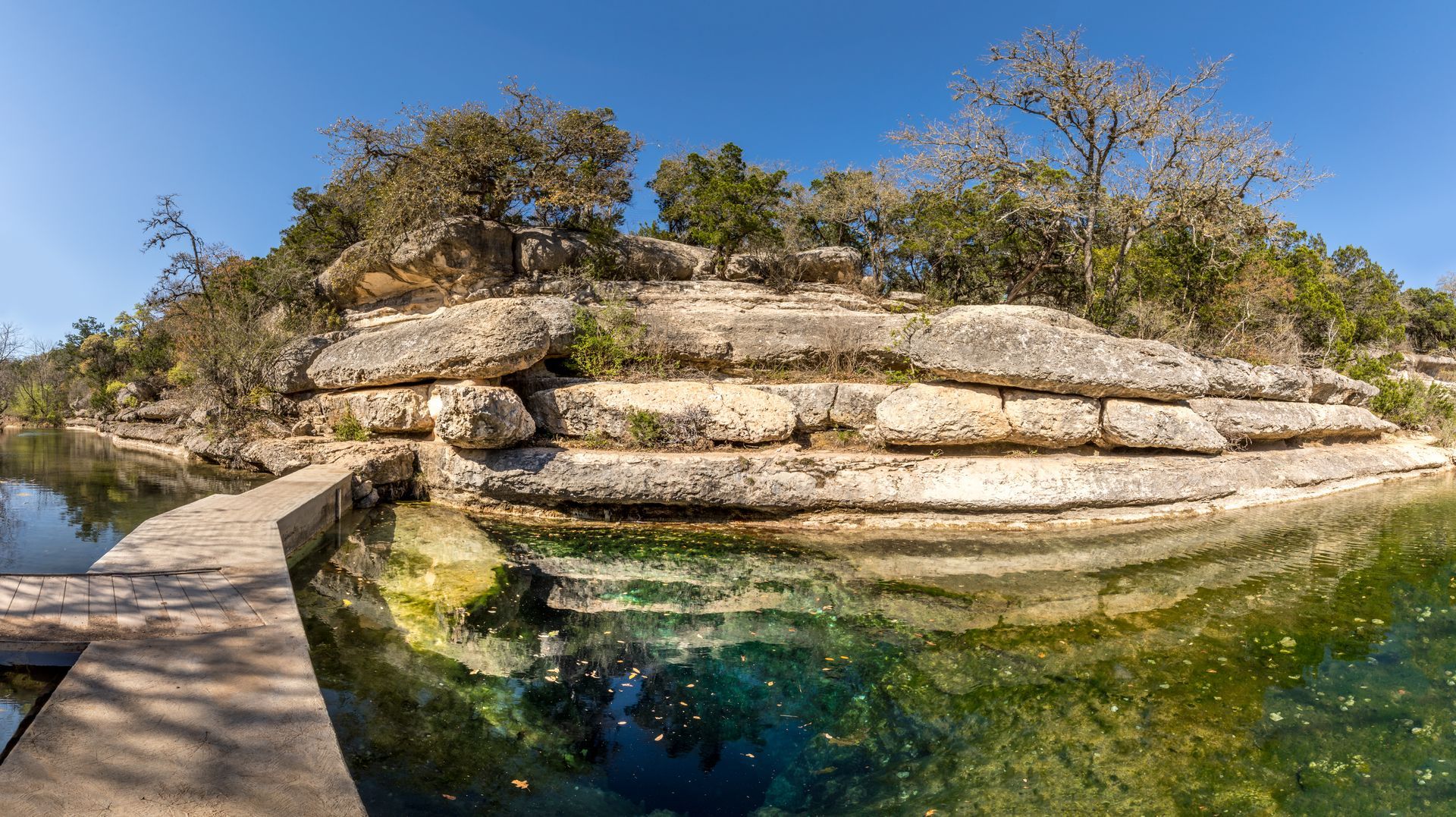 A wooden walkway leading to a body of water surrounded by rocks and trees.