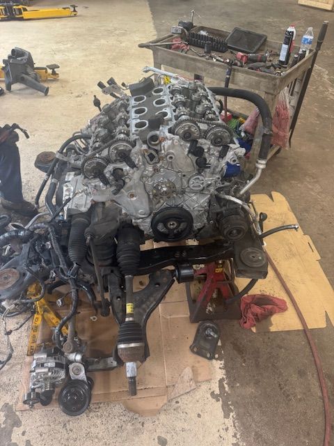 Engine on the floor in a garage; front suspension attached, surrounded by parts, tools, and a parts cart. | Loyola Service