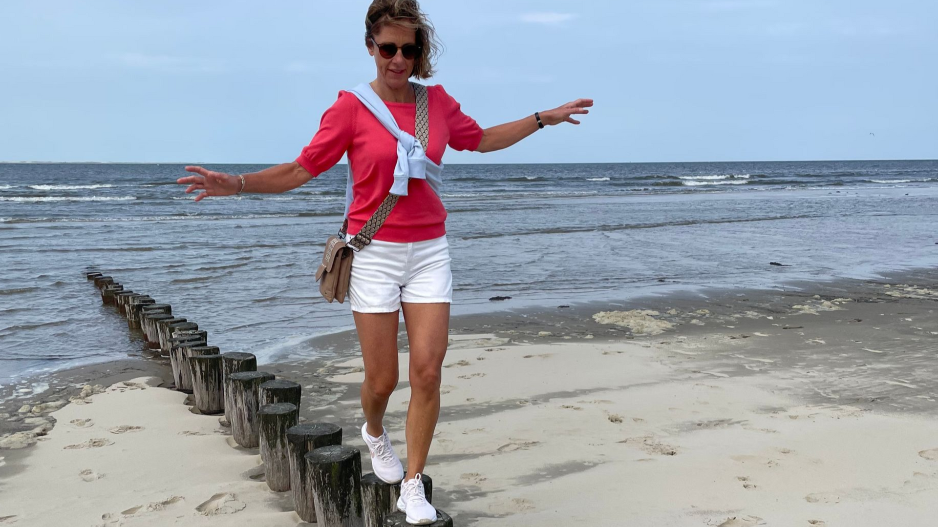 Vrouw balanceren op houten paaltjes op het strand met armen gespreid