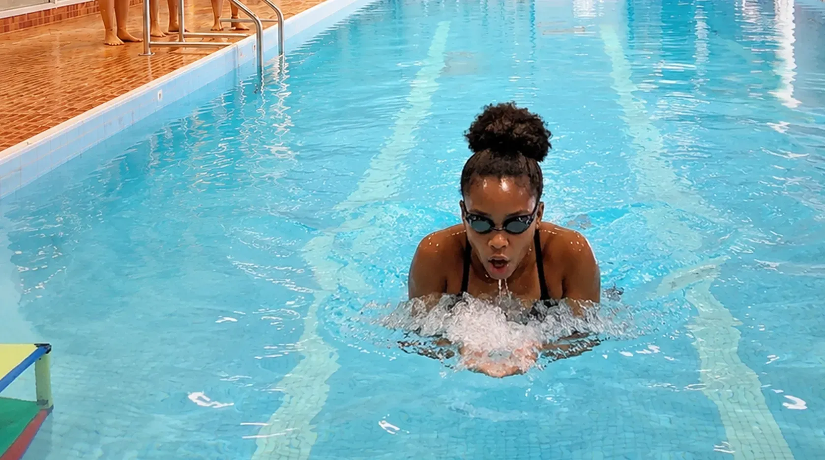 Person swimming in a bright blue pool, creating splashes near the center.