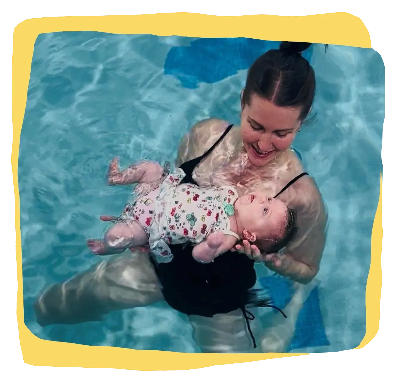 Woman holding an infant in a swimming pool, both floating in clear blue water.