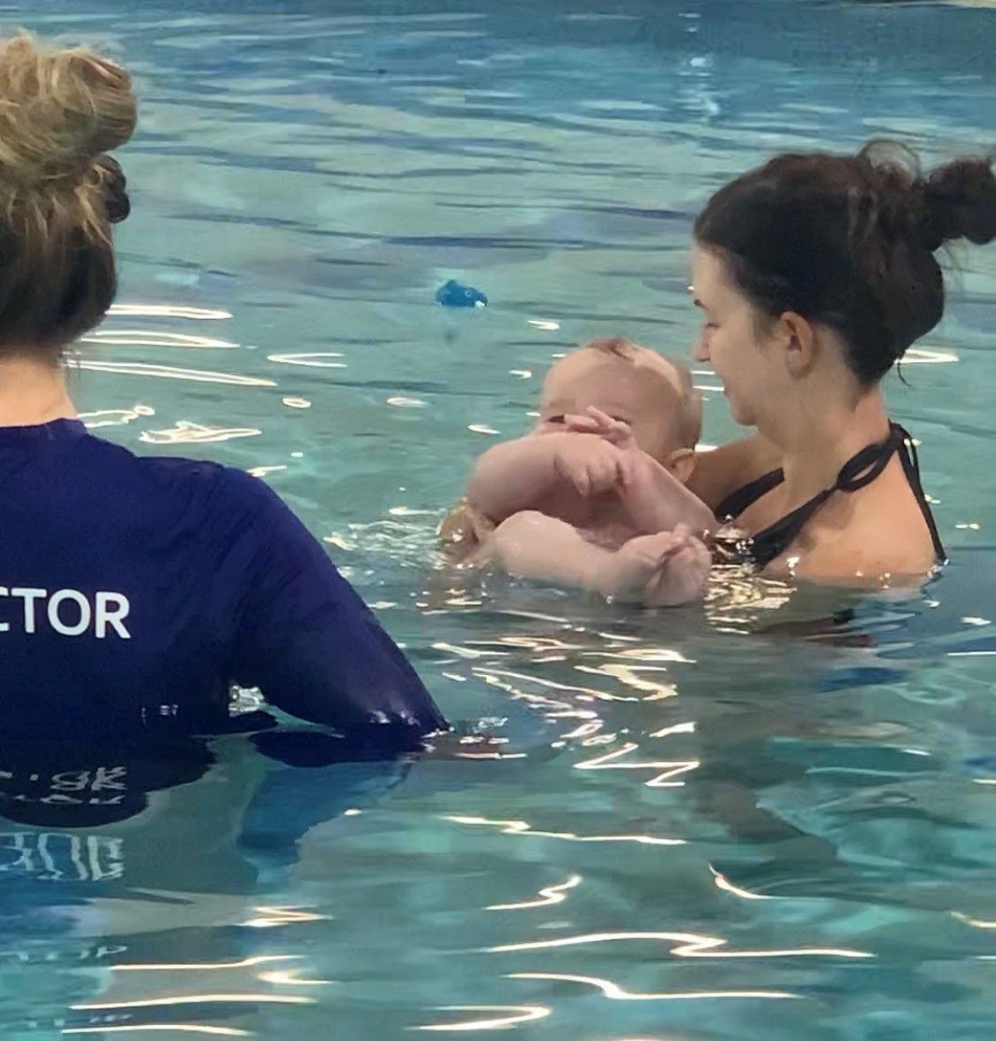 Swimming instructor helping a baby in a pool while another adult watches nearby
