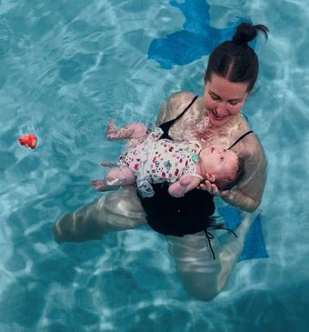 Woman holding a baby in a swimming pool, both floating in clear blue water