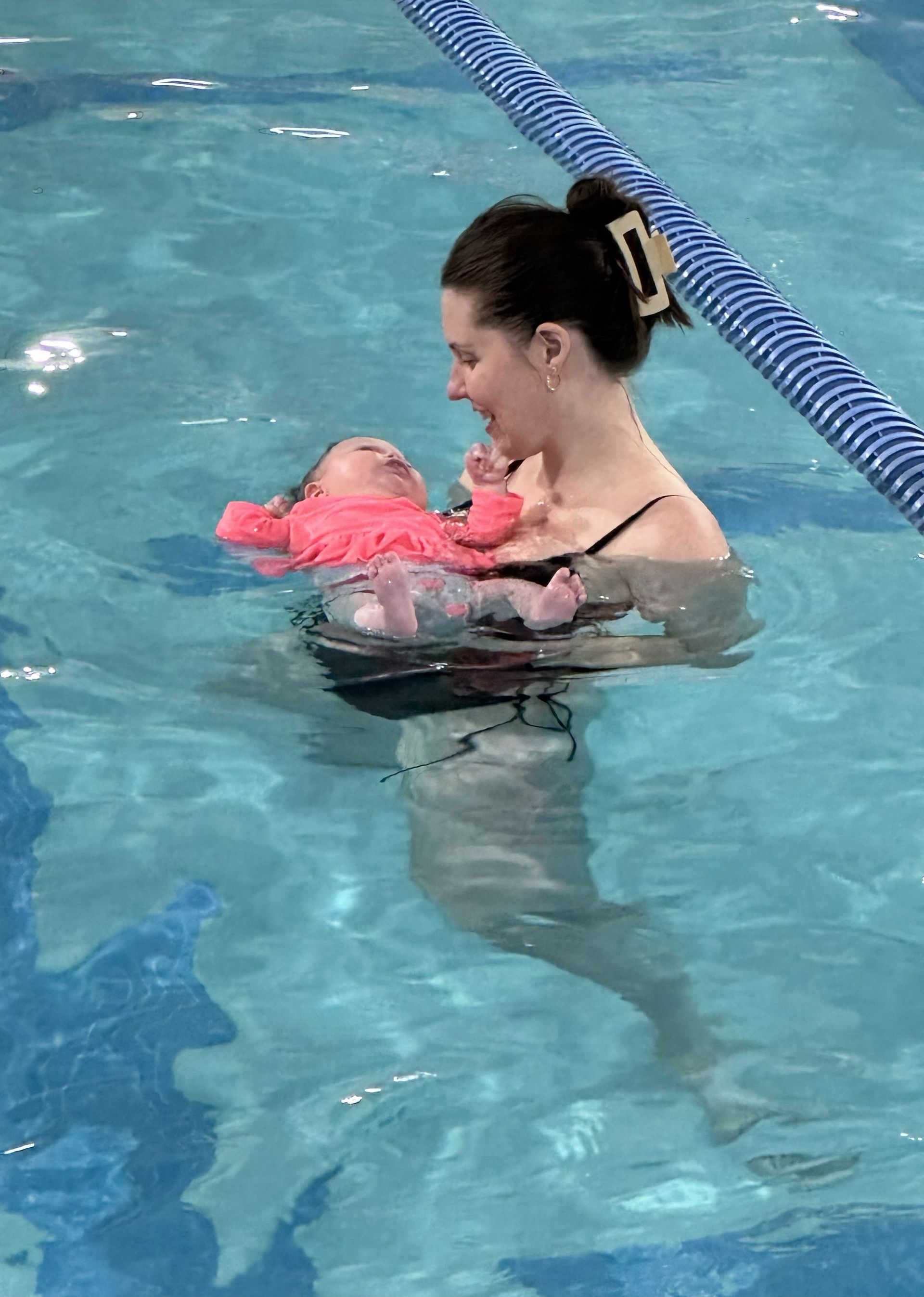 Woman holding a baby in a swimming pool with blue lane ropes nearby