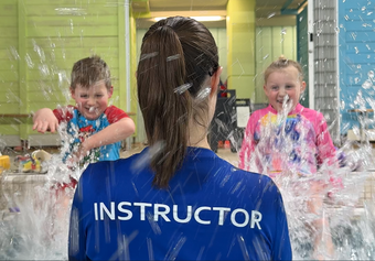 Instructor facing two children splashing water in a pool or water play area