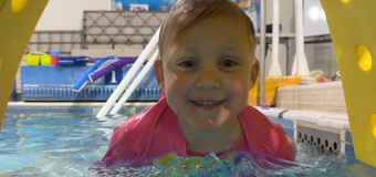 Smiling child in a pink flotation vest in a swimming pool tunnel