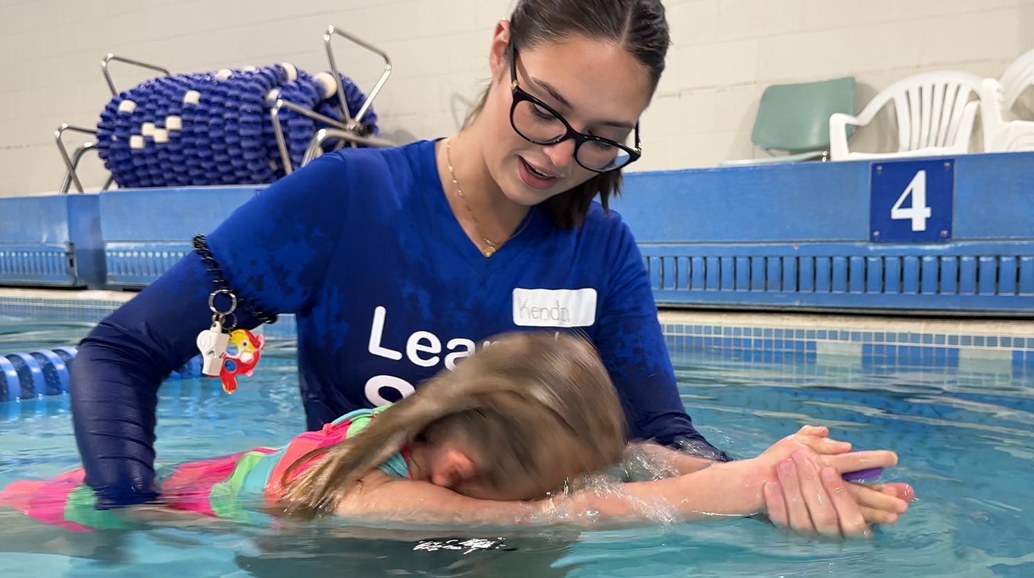 Swimming instructor helping a child practice in an indoor pool