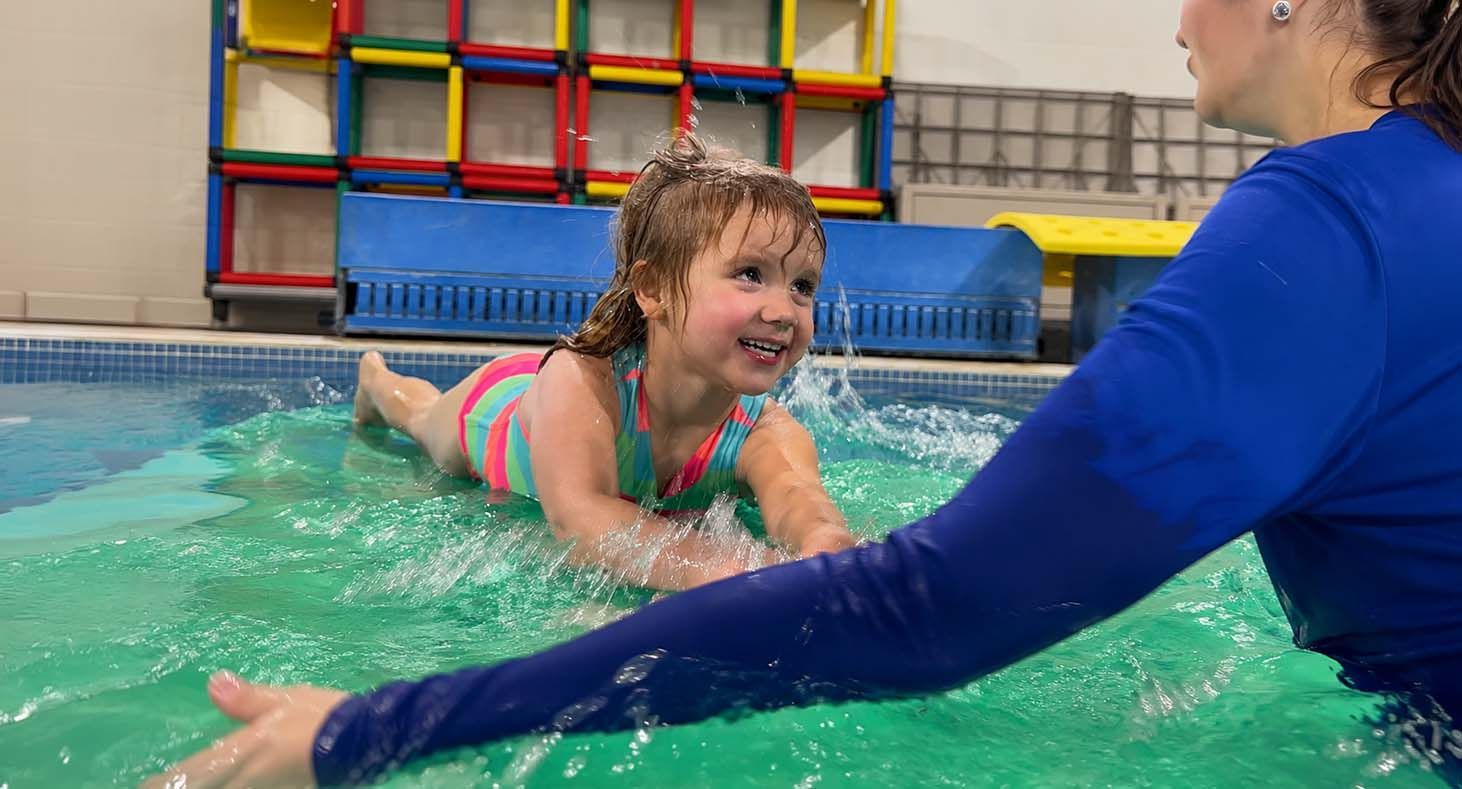 Pool rescue training with a lifeguard reaching toward a swimmer using a red rescue float