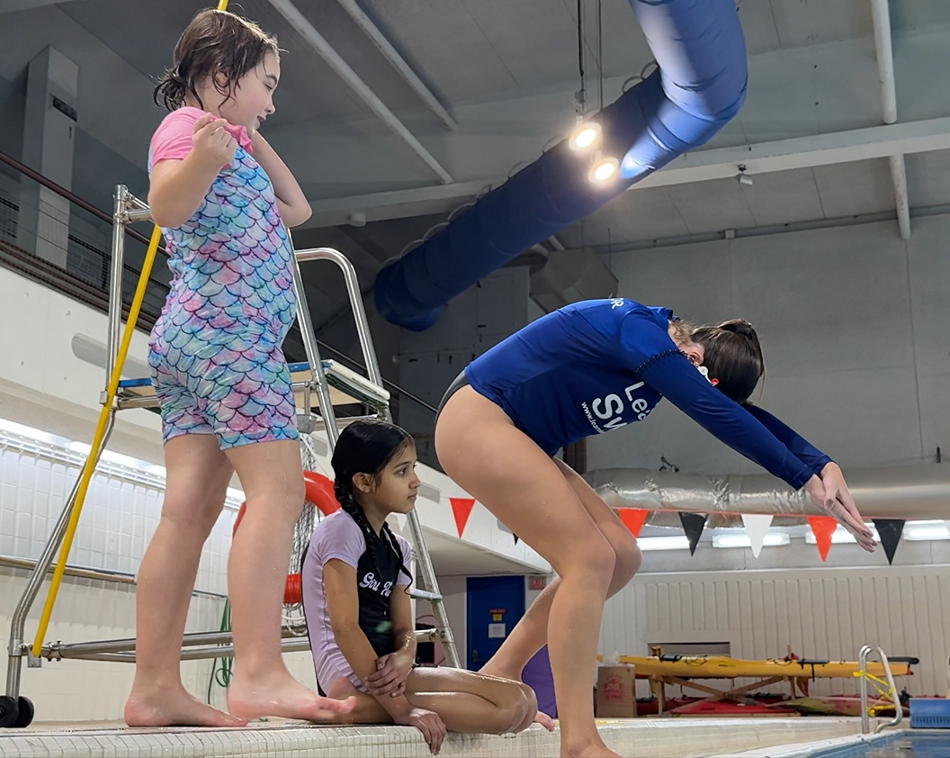 Children on a pool deck doing a swim lesson, preparing to enter the water
