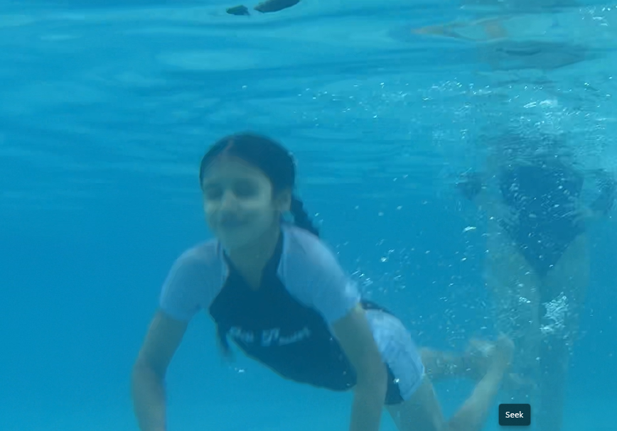 Child swimming underwater in a blue pool, reaching forward with bubbles behind them