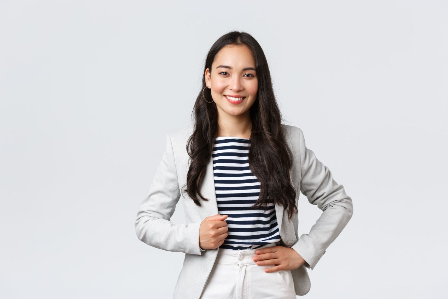 A woman in a suit and striped shirt is standing with her hands on her hips.