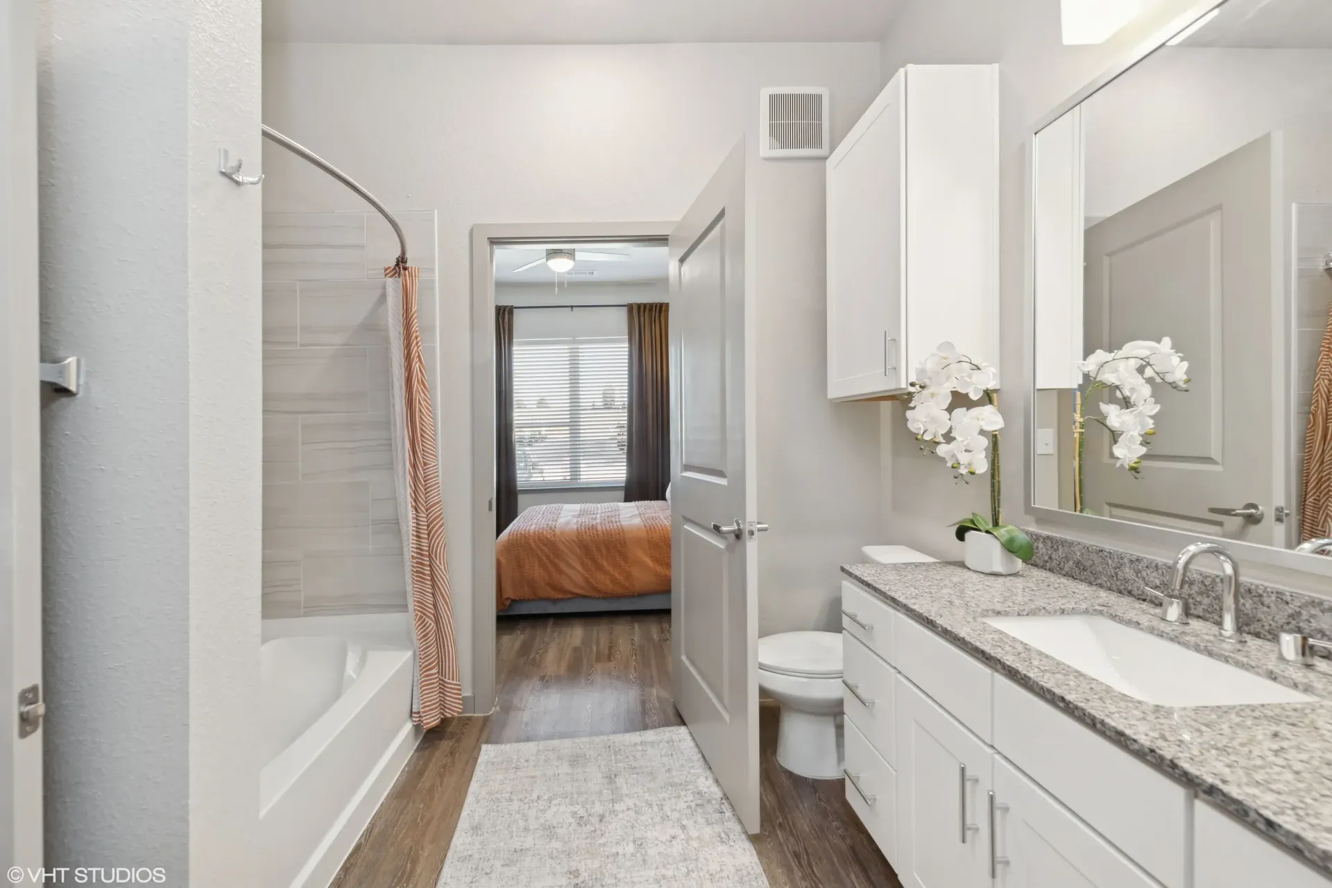 Bathroom in an apartment with a white vanity, granite countertop, mirror, and a tub/shower.