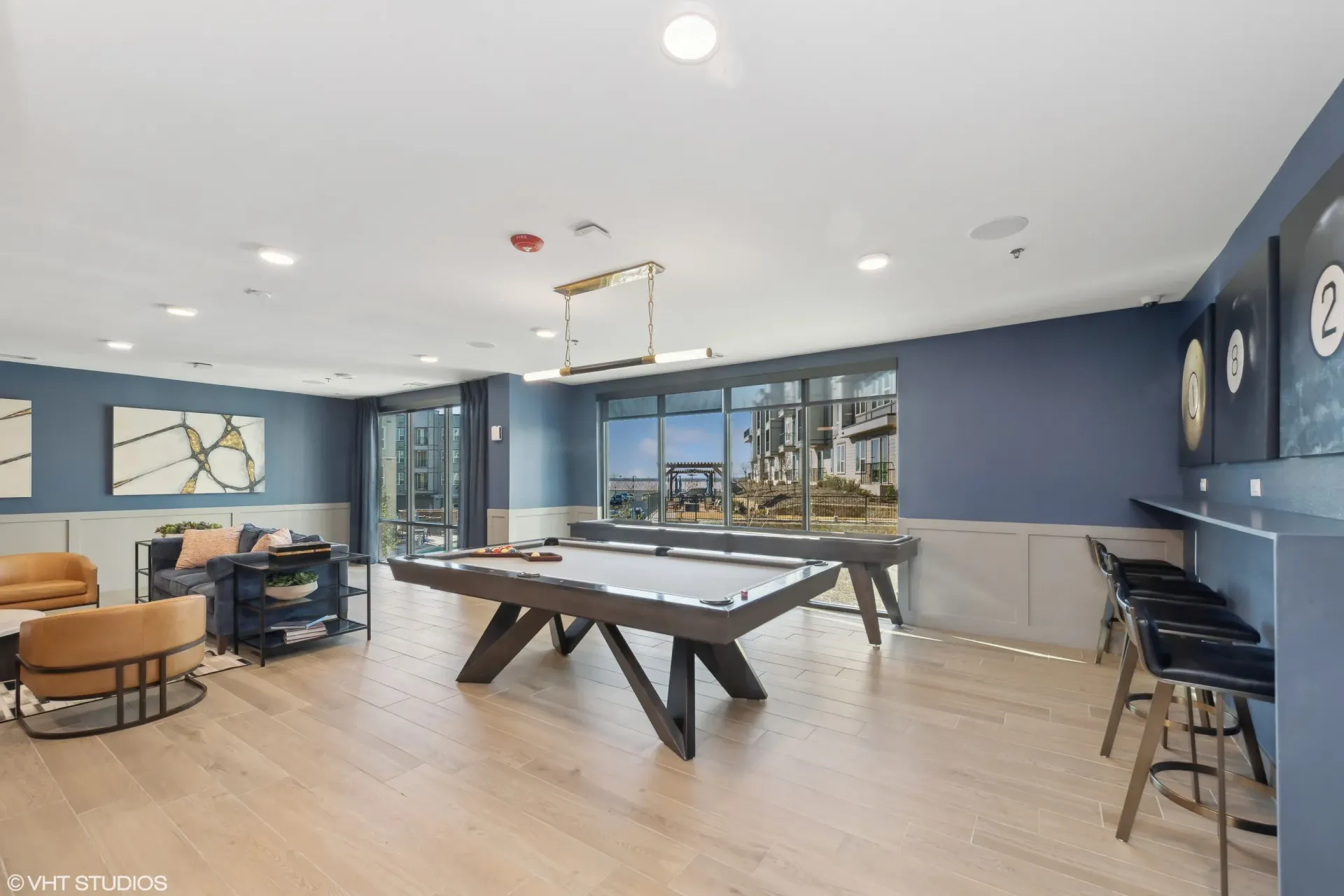 Contemporary community lounge with a pool table, seating area, and large windows.