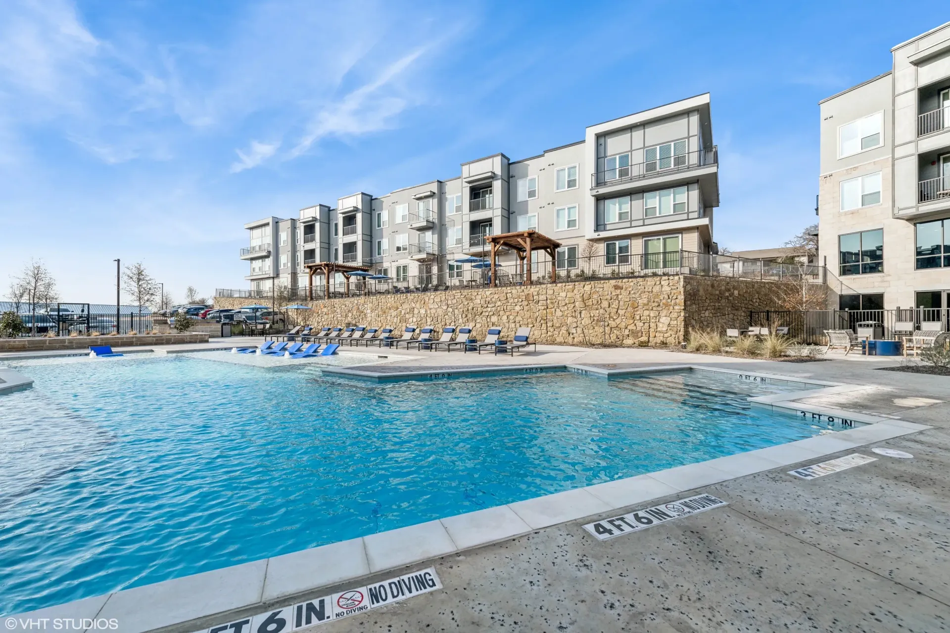 Outdoor community pool at an apartment complex with lounge chairs and stone terrace.