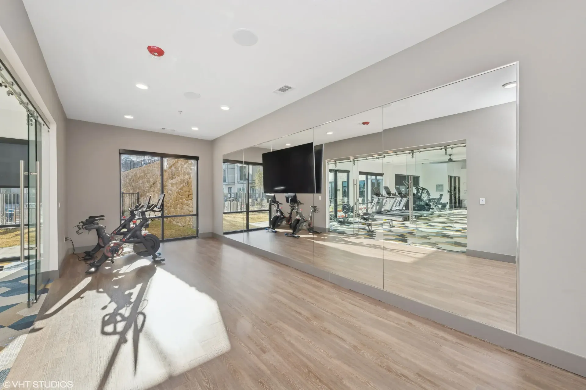 Bright fitness center with cardio bikes, a wall of mirrors, and a TV.