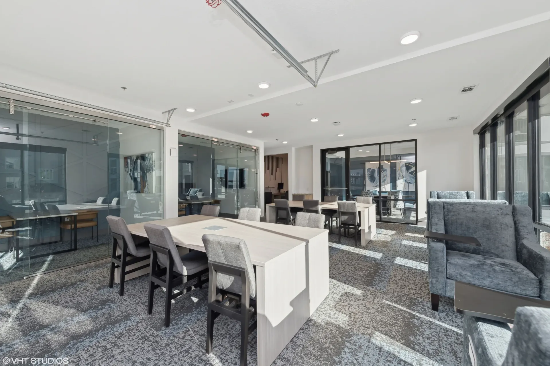 Modern community lounge with glass walls, tables, and lounge chairs.