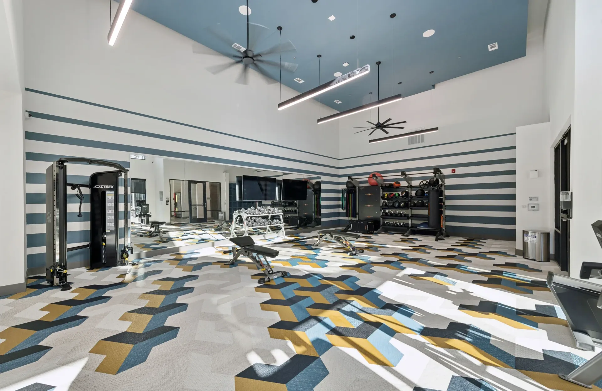 Interior gym with weight machines, free weights, and cardio equipment; striped walls.